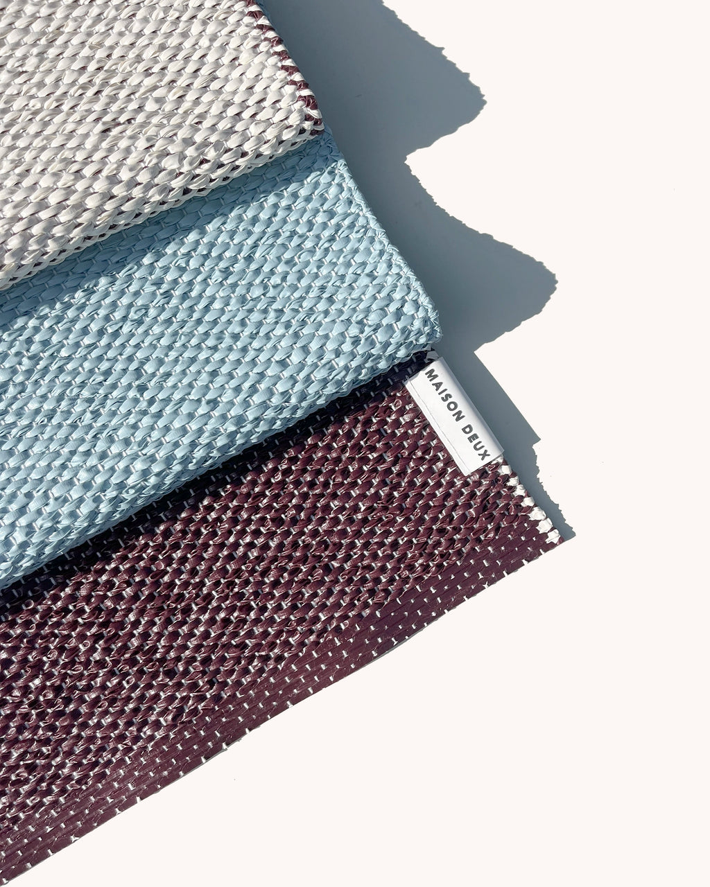 Close-up of folded burgundy, blue and cream color block vinyl doormat showing woven texture