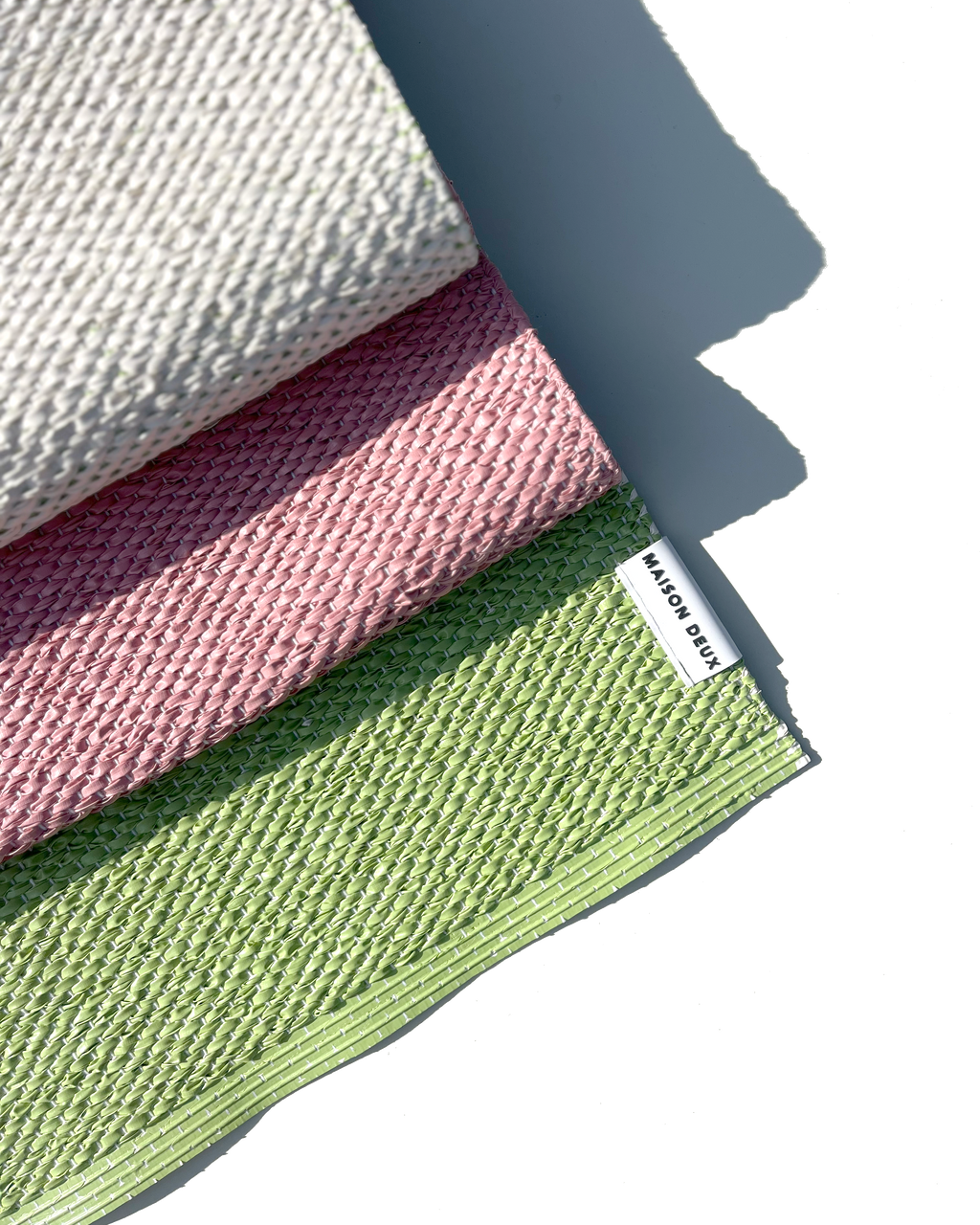 Close-up of folded pink, green and cream color block vinyl doormat showing woven texture