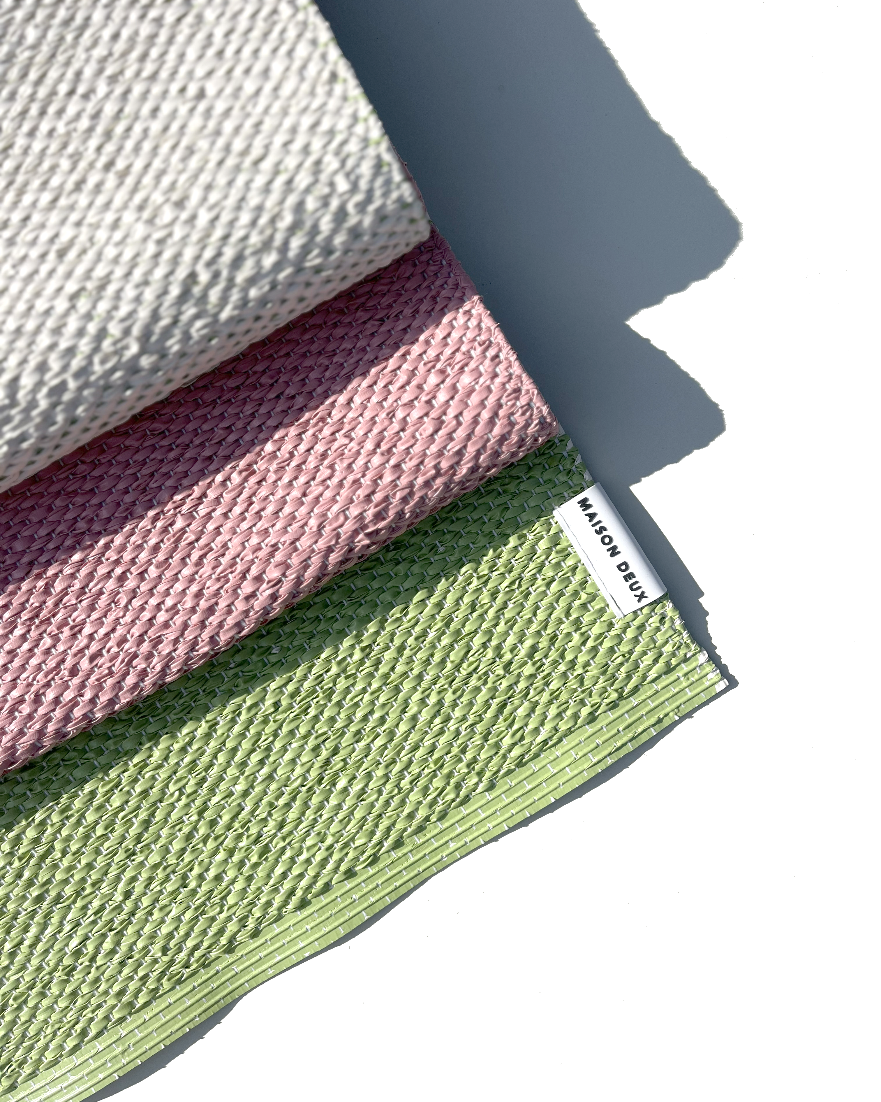 Close-up of folded pink, green and cream color block vinyl doormat showing woven texture