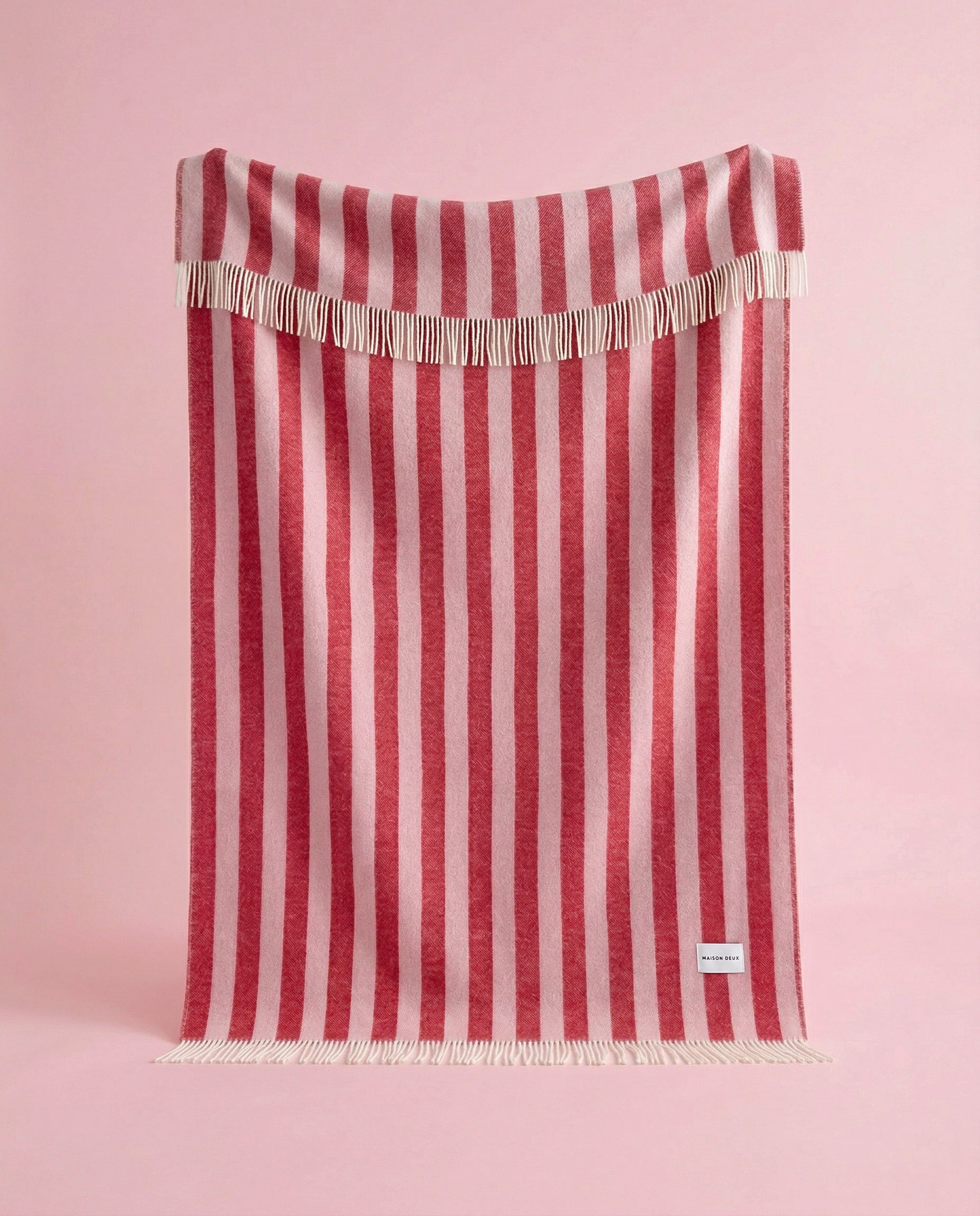 Pink and cherry red striped wool blanket hanging against pink background
