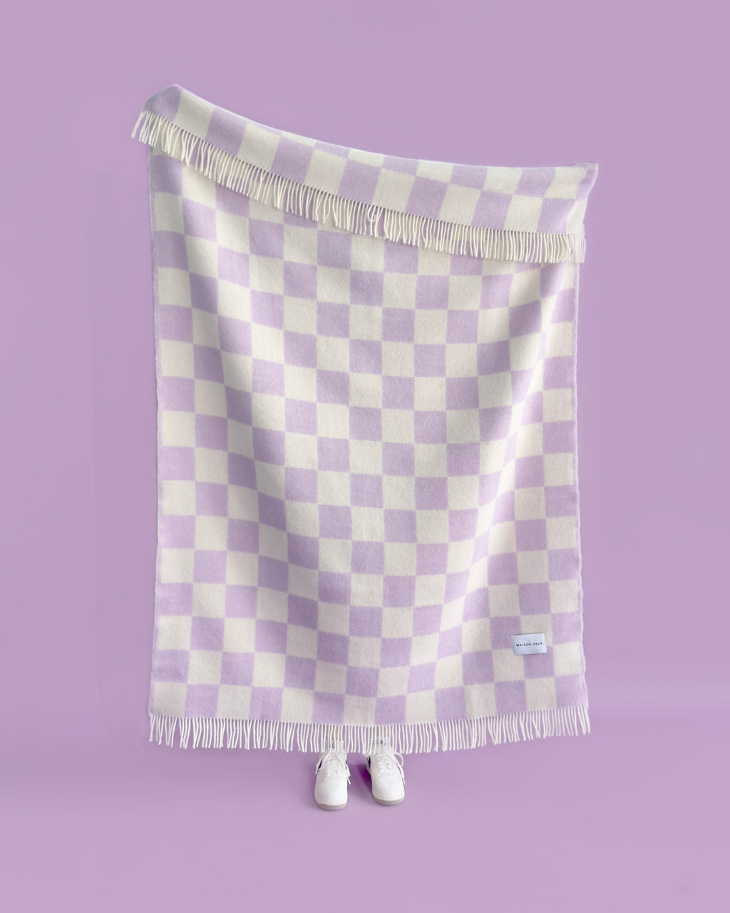 Lilac and white checkerboard wool throw hanging against purple background, held up by a person
