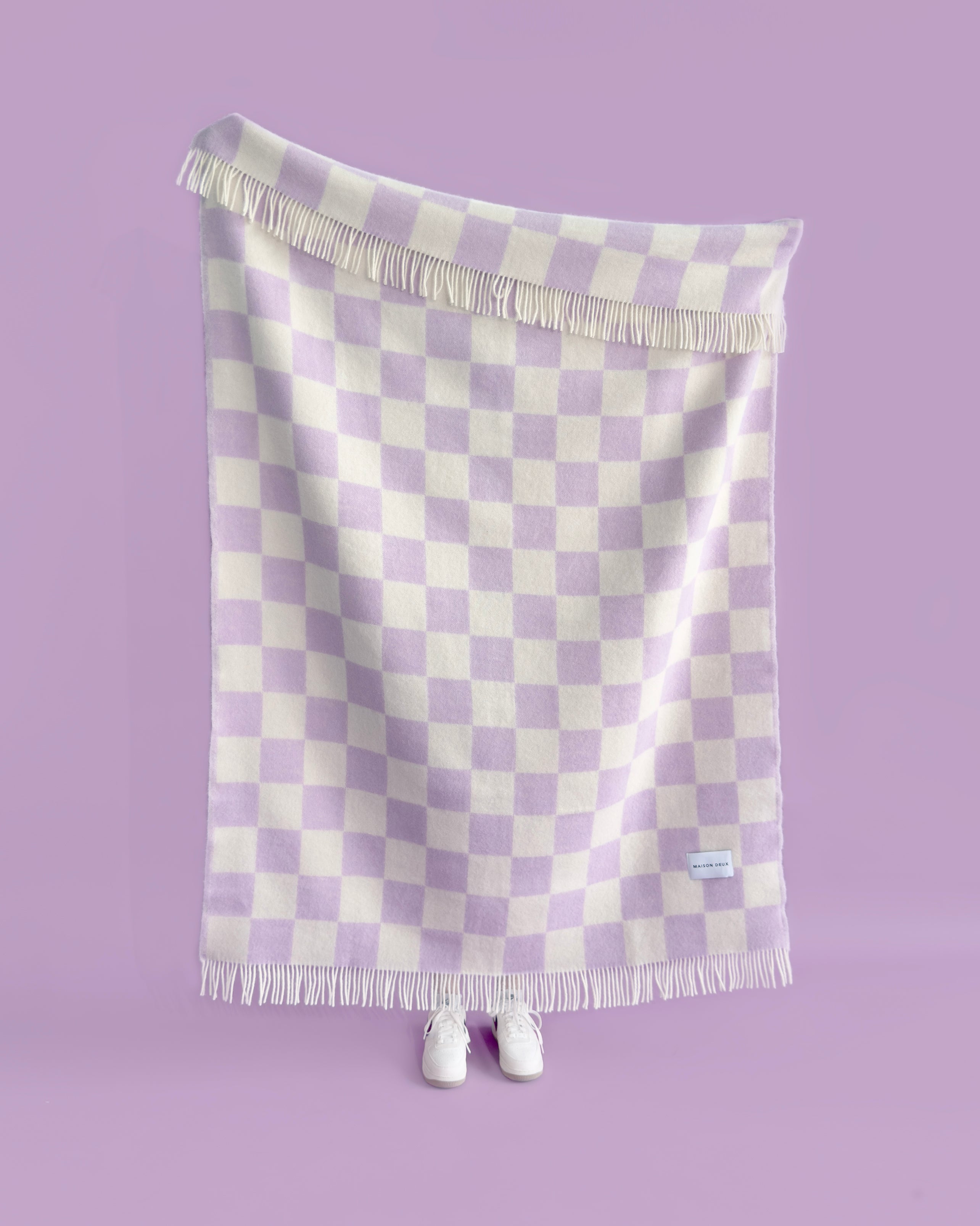 Lilac and white checkerboard wool throw hanging against purple background, held up by a person