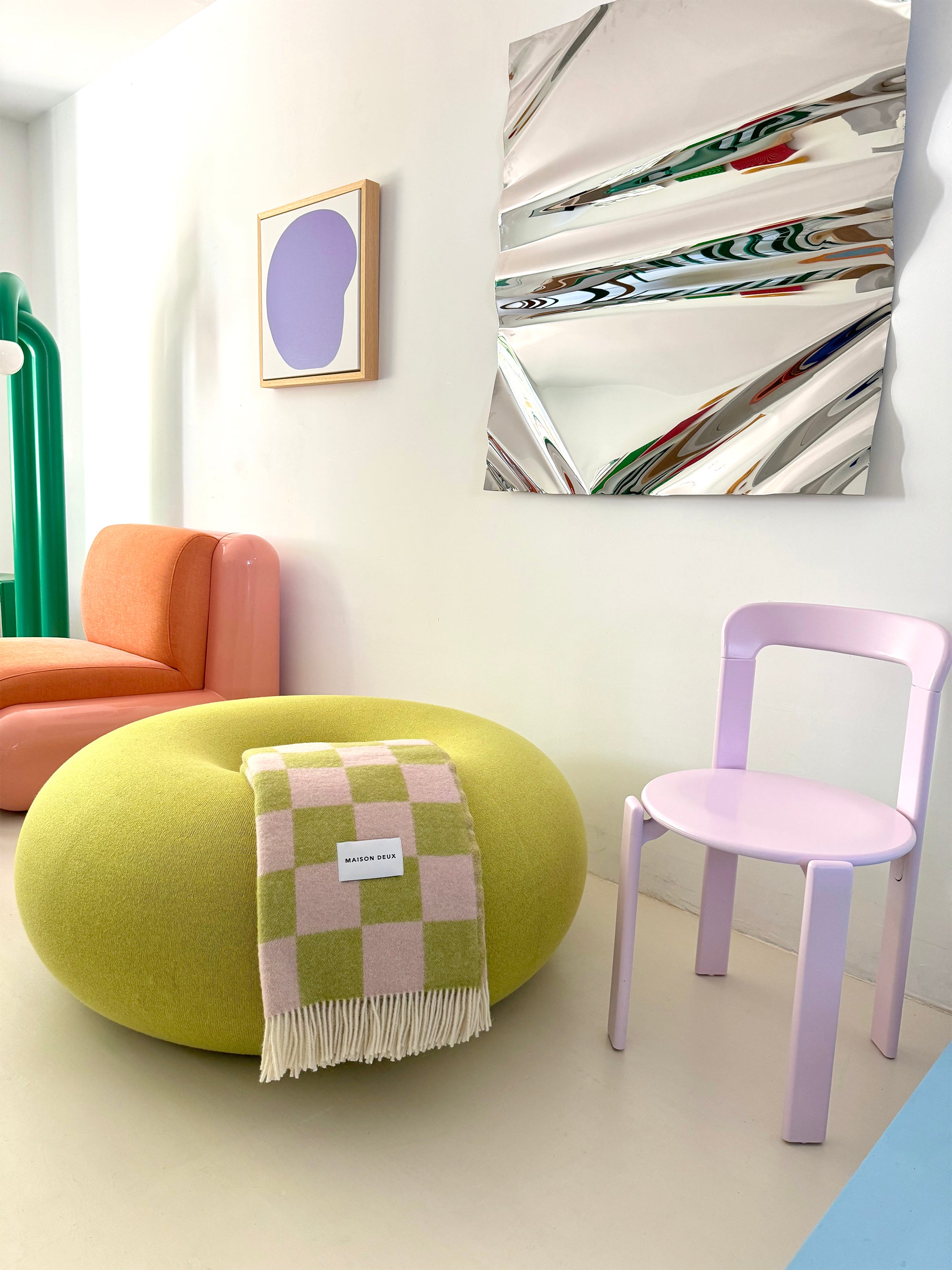 Lime green and pink checkerboard wool blanket plaid draped over pouf in styled room
