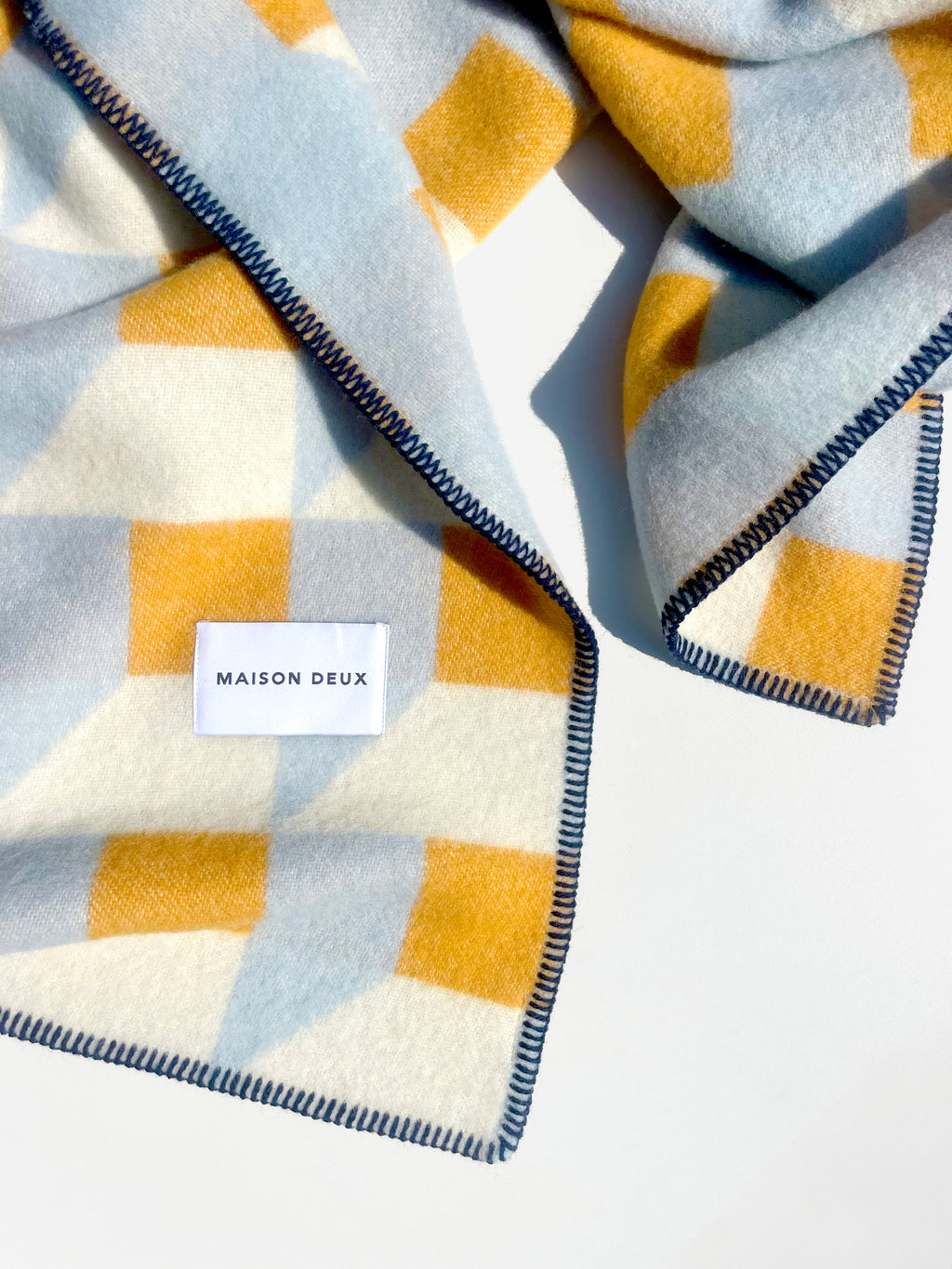 Close-up of folded light blue and honey yellow geometric wool blanket
