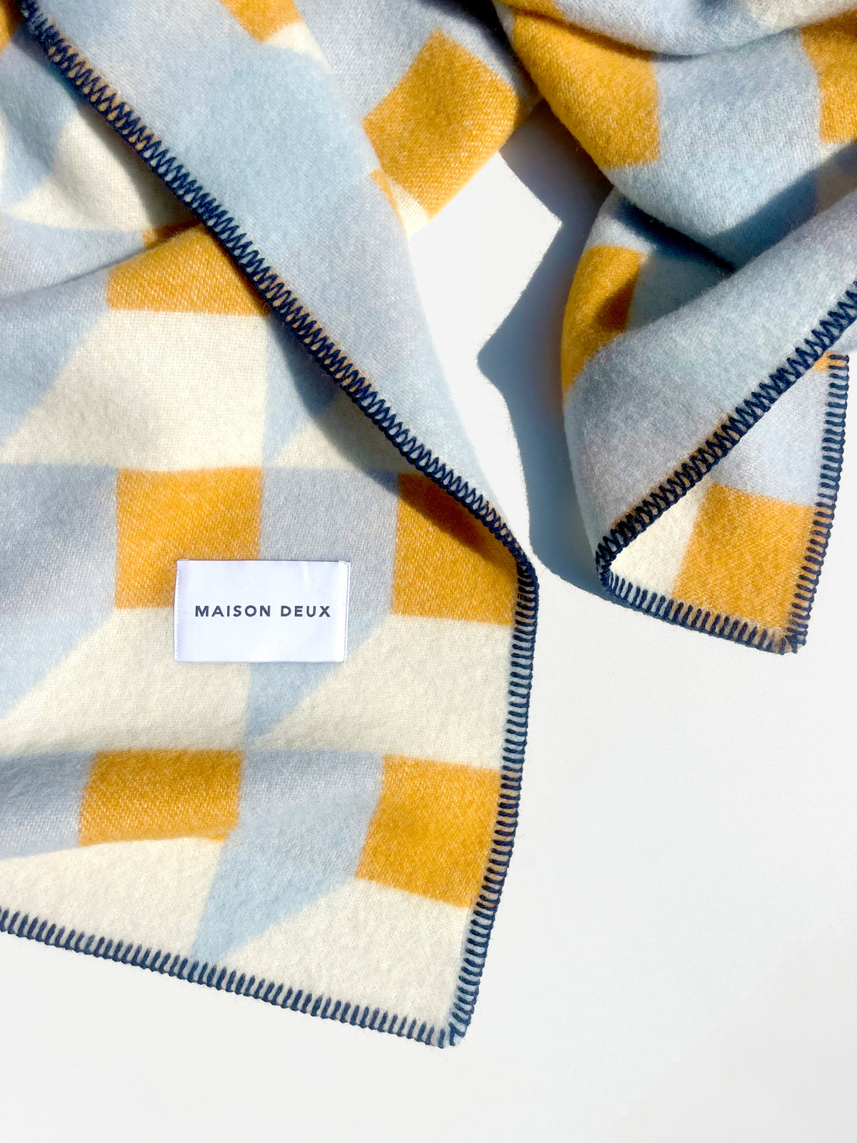 Close-up of folded light blue and honey yellow geometric wool blanket

