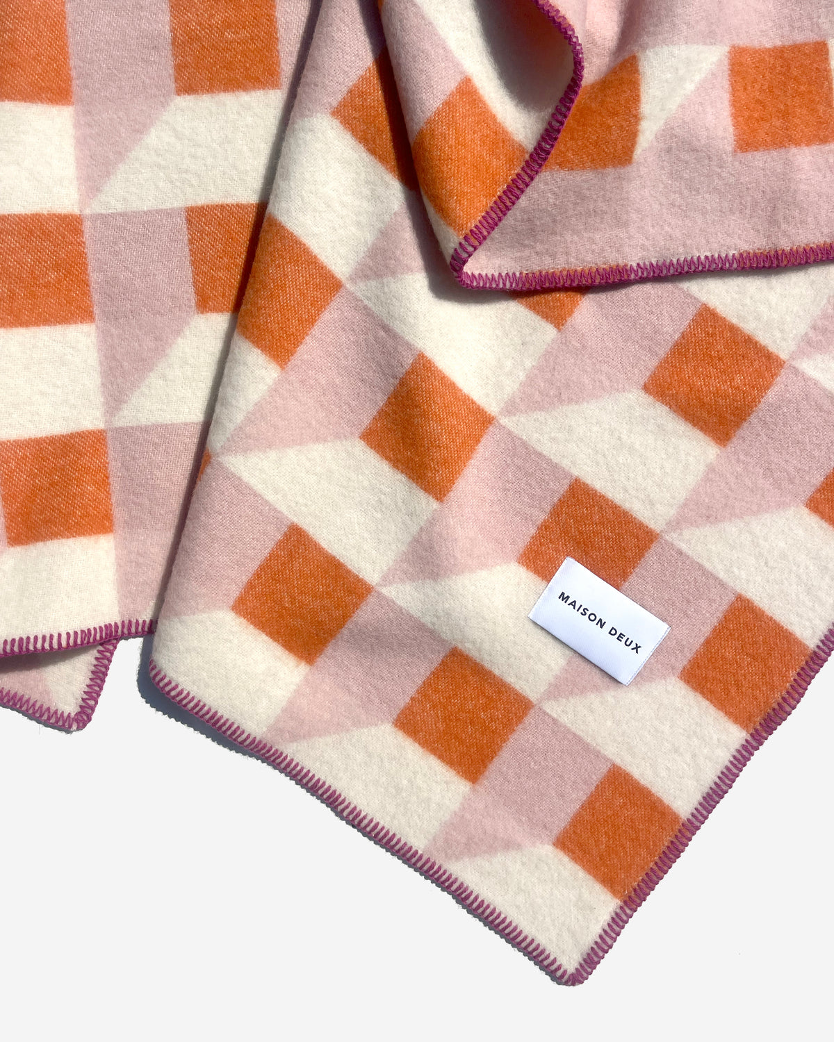 Close-up of folded pink and carrot orange geometric wool blanket

