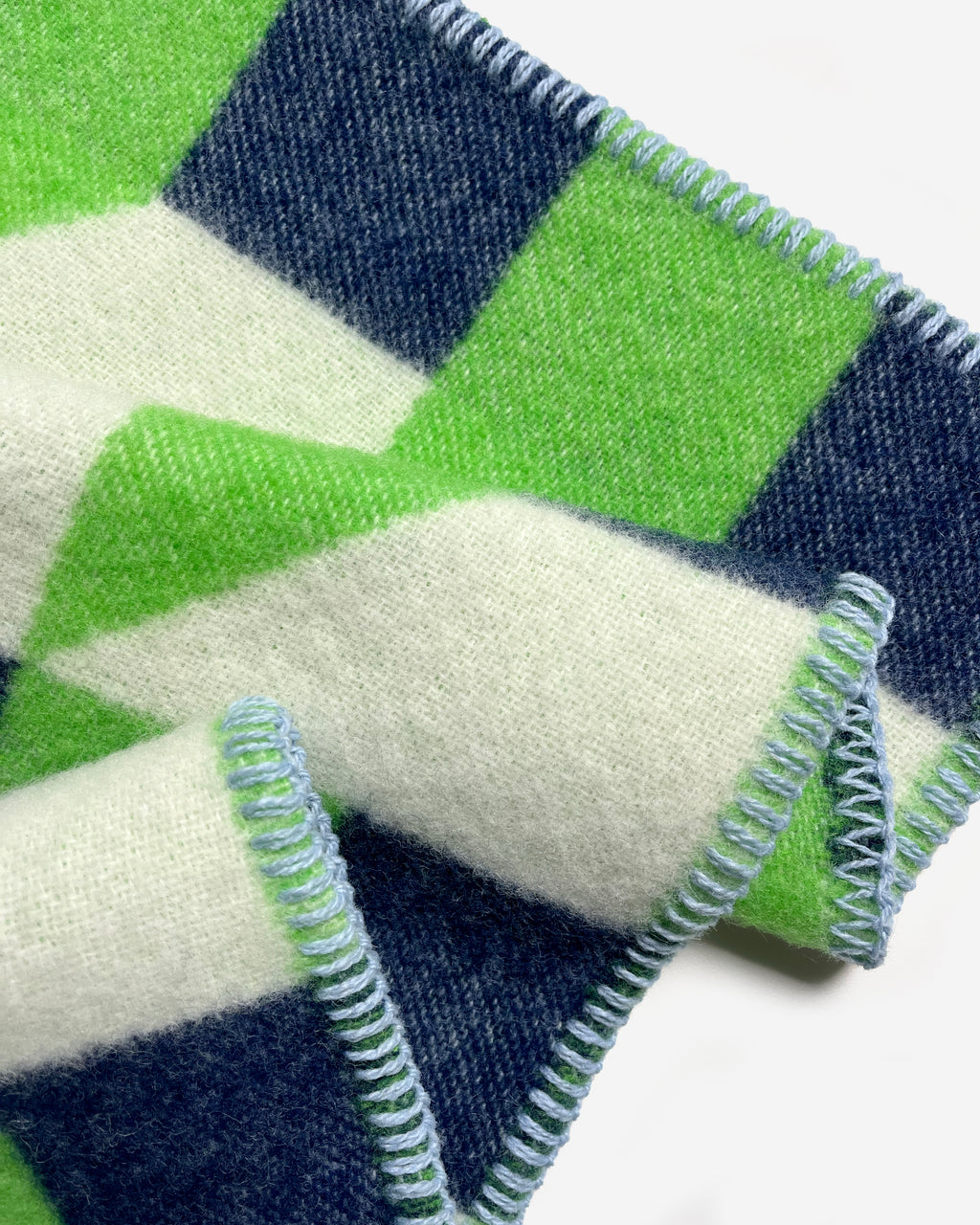Close-up of folded apple green and navy geometric wool plaid with stitched edge
