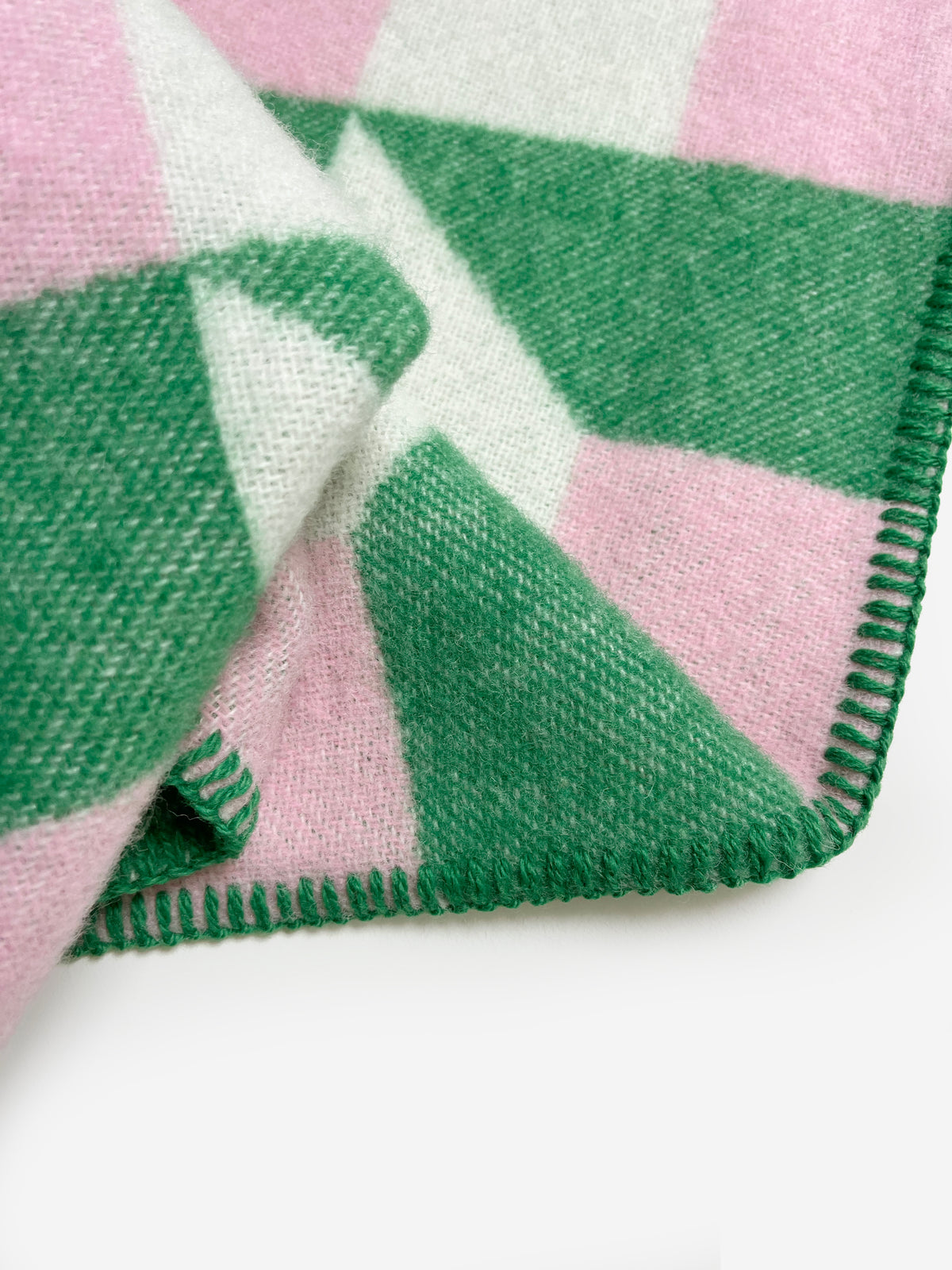 Close-up of folded grass green and pink geometric wool plaid with stitched edge
