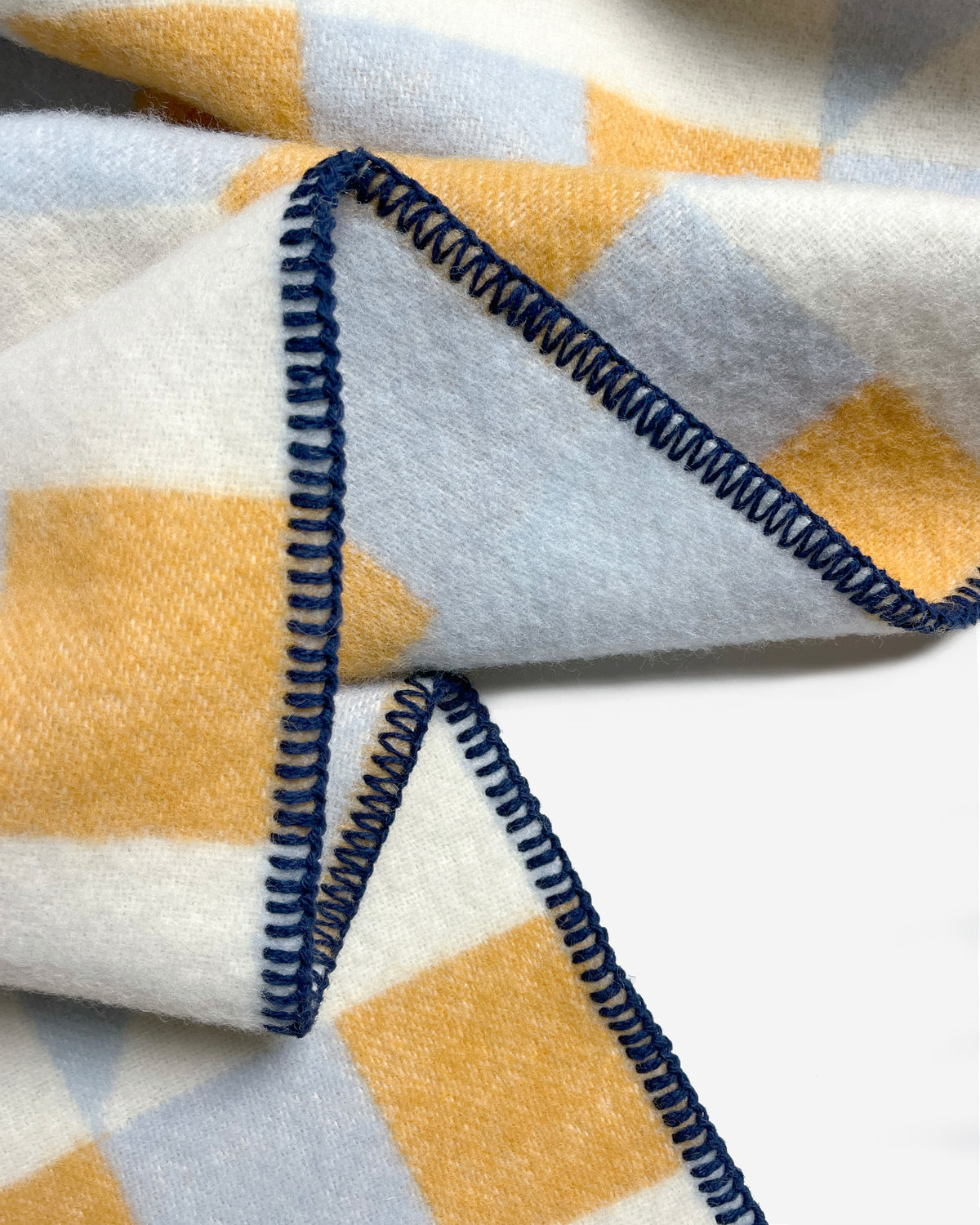 Close-up of folded light blue and honey yellow geometric wool plaid with stitched edge
