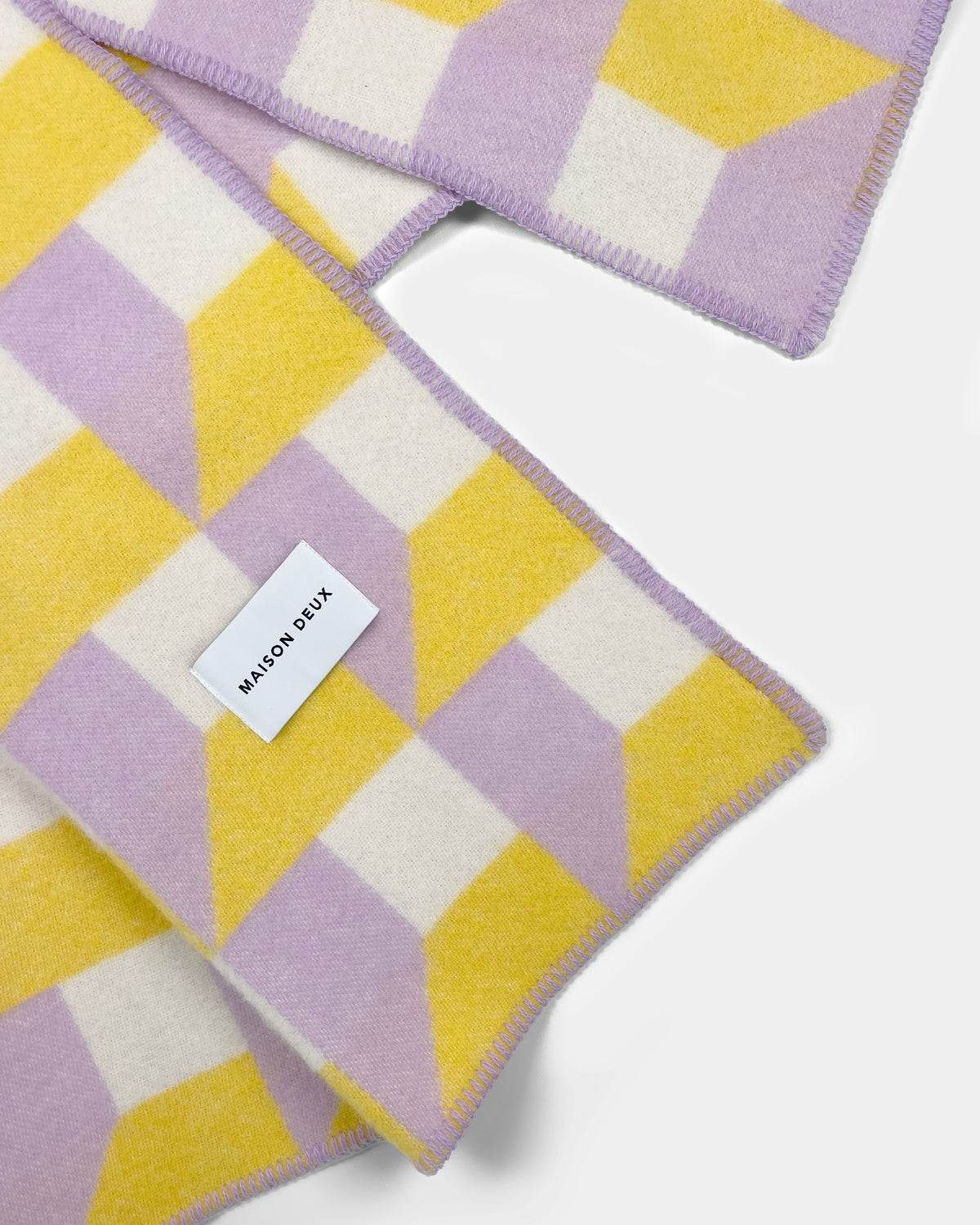 Close-up of folded lilac and yellow geometric wool plaid with stitched edge
