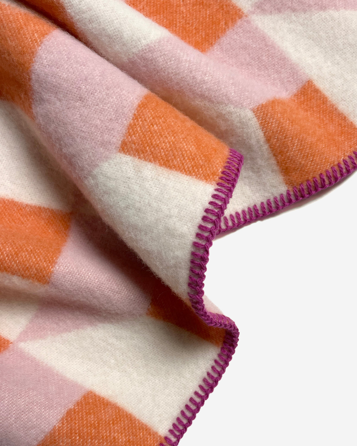 Close-up of folded pink and carrot orange geometric wool plaid with stitched edge
