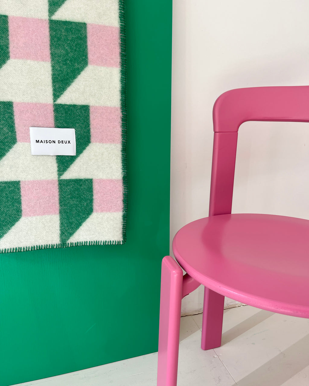 Grass green and pink geometric wool throw hanging on wall next to chair
