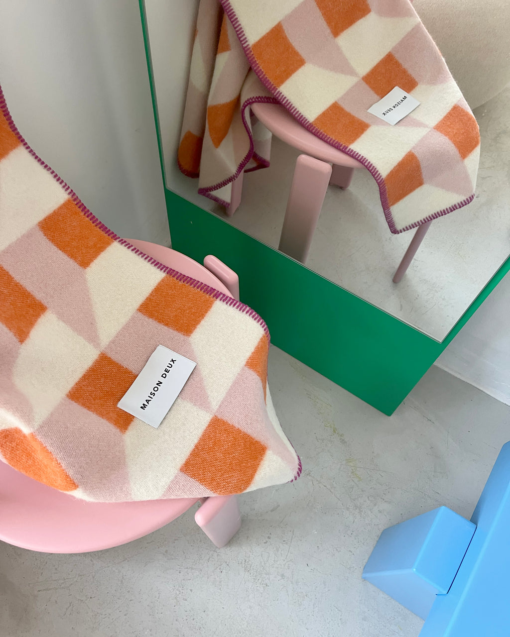 Pink and carrot orange geometric wool throw draped over chair with mirror reflection
