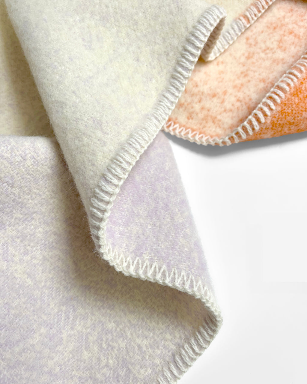 Close-up of folded orange and lilac gradient wool plaid with stitched edge
