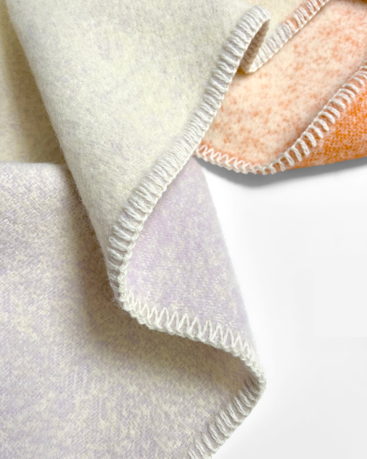 Close-up of folded orange and lilac gradient wool plaid with stitched edge
