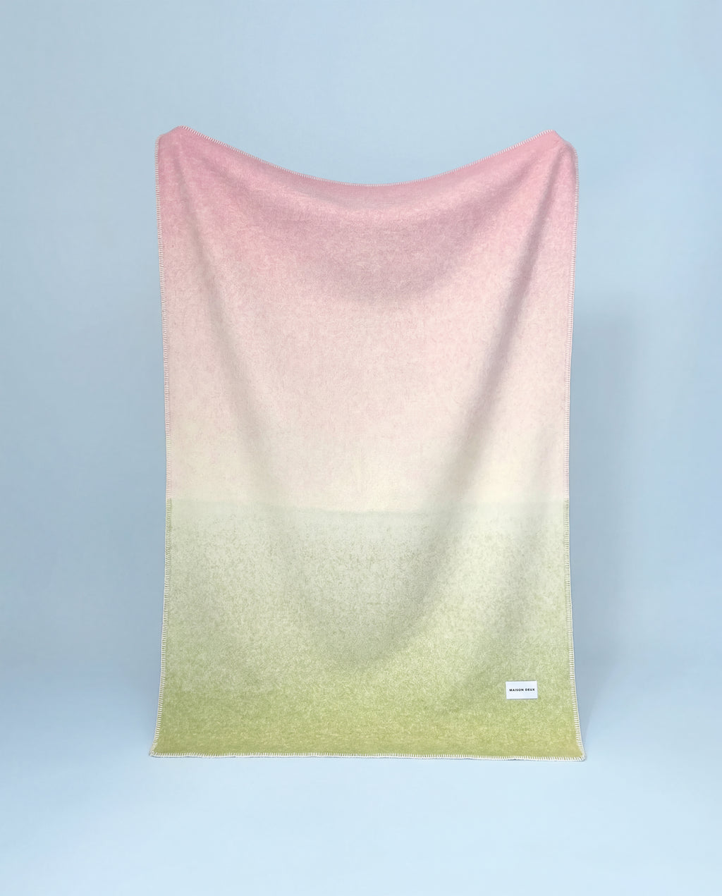 Pink to kiwi green gradient wool throw hanging against blue background
