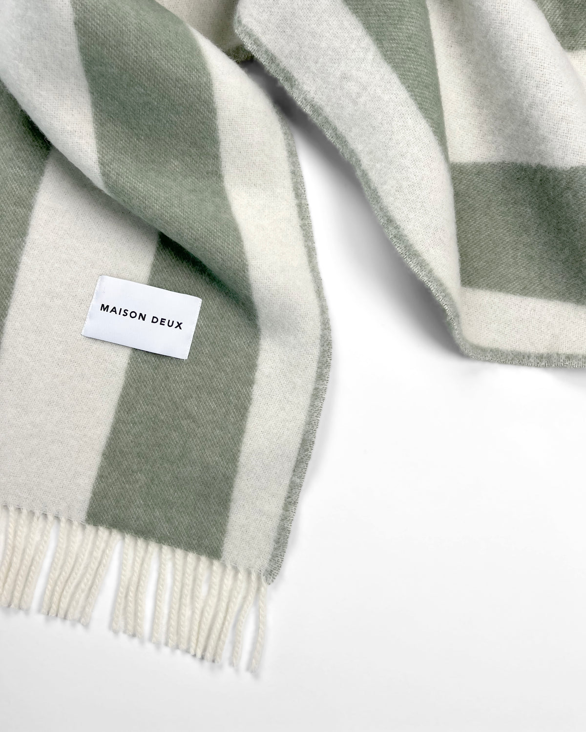 Close-up of sage green and white striped wool plaid with fringe

