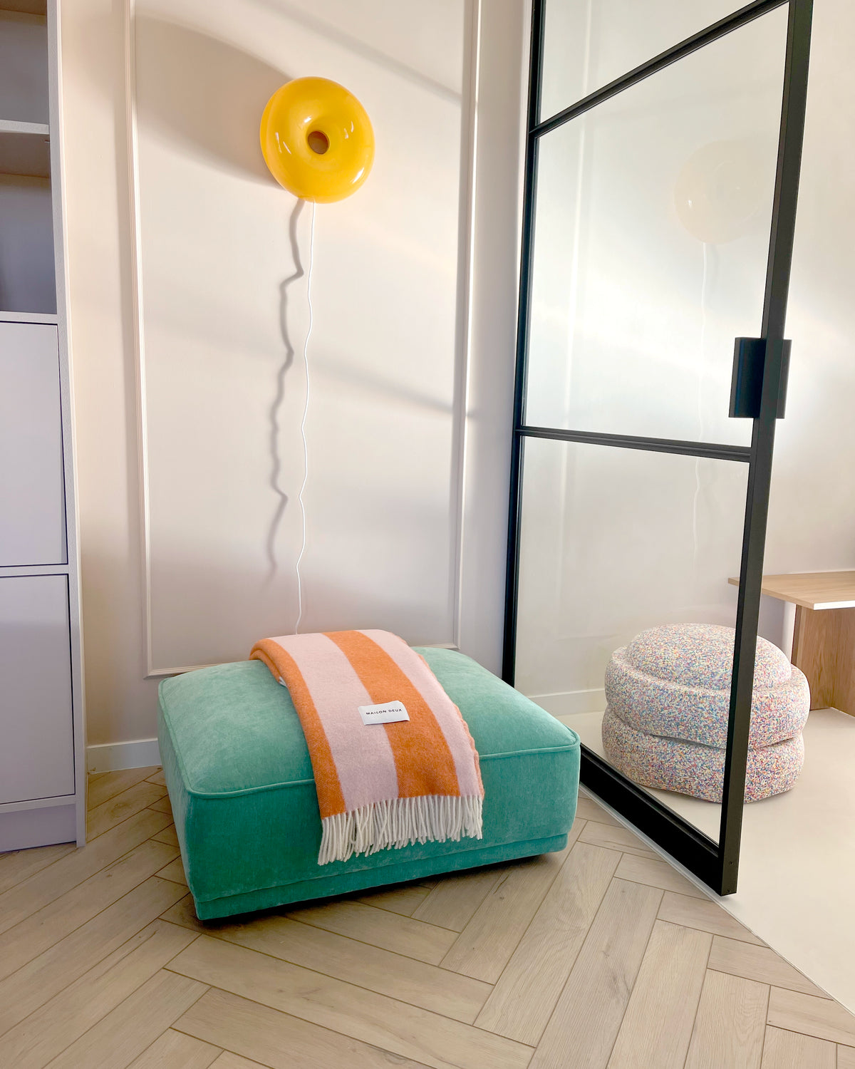 Pink and carrot orange striped wool throw draped over pouf in styled room

