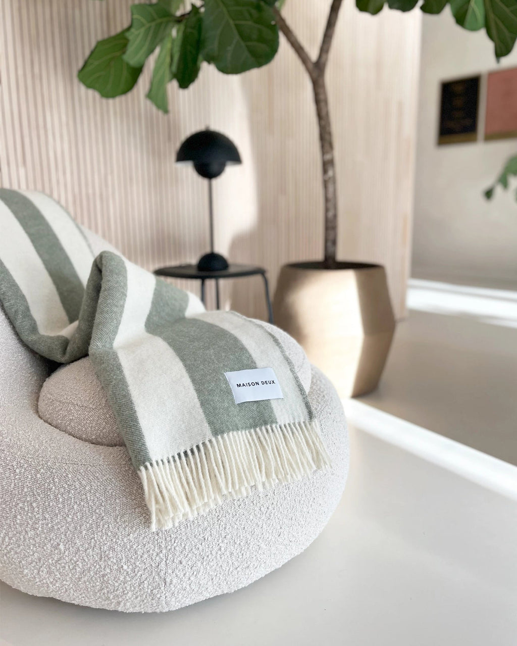Sage green and white striped wool throw draped over armchair in styled room
