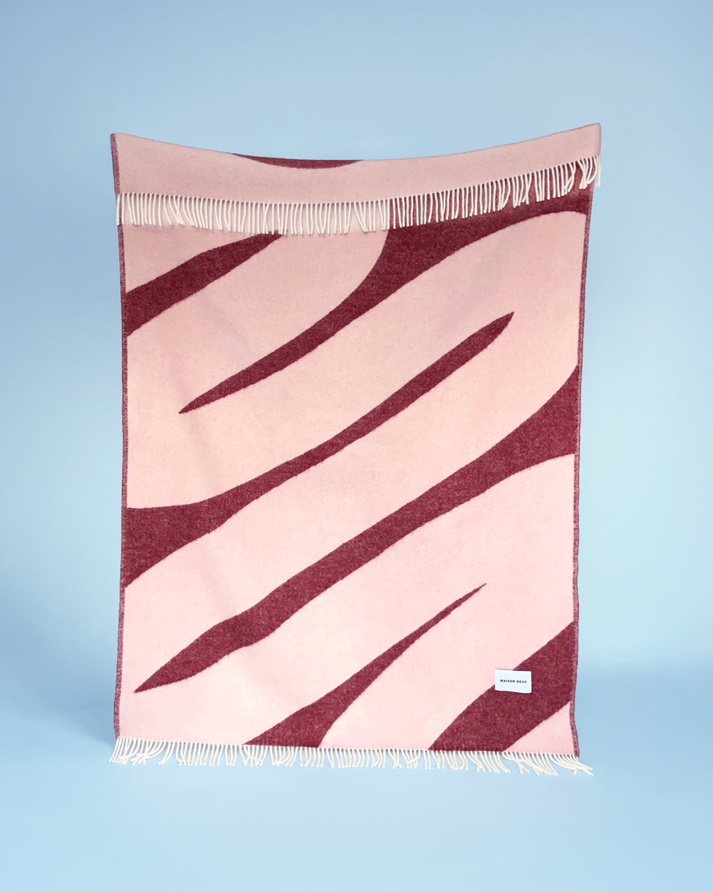 Pink and bordeaux swirl wool throw hanging against blue background
