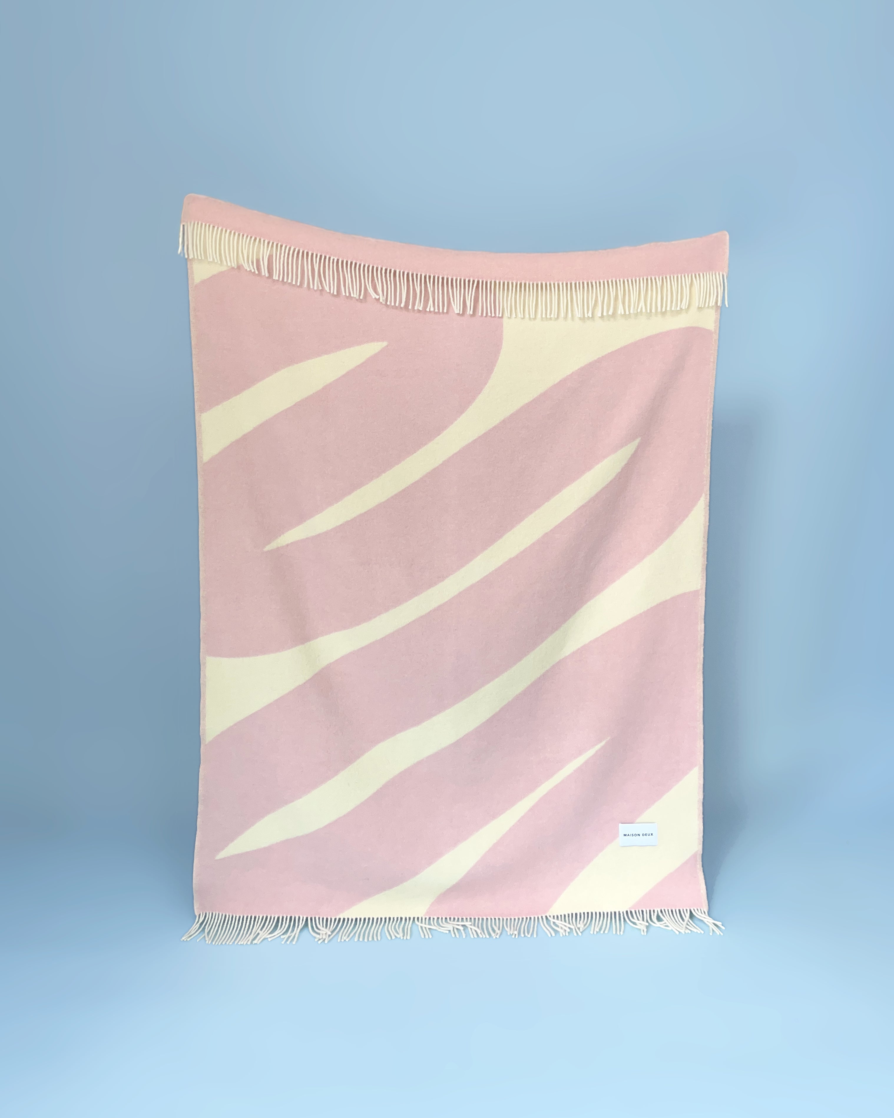 Pink and butter yellow swirl wool throw hanging against blue background
