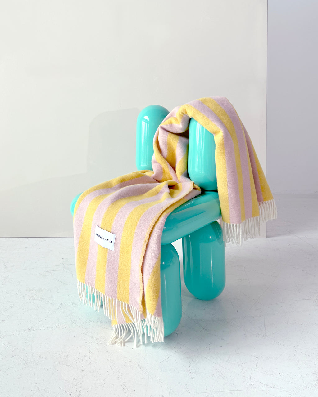 Pink and yellow striped wool throw draped over teal chair
