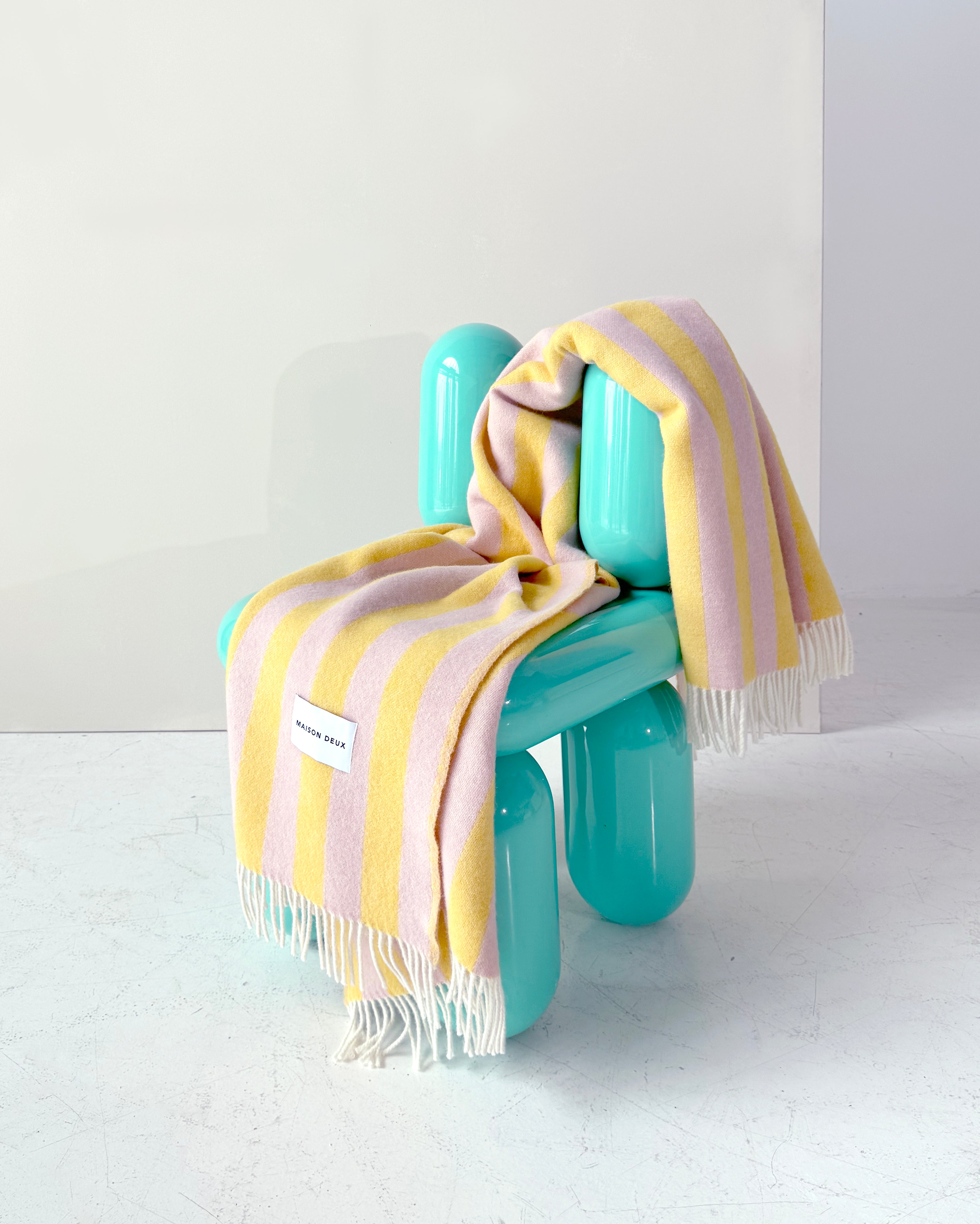 Pink and yellow striped wool throw draped over teal chair
