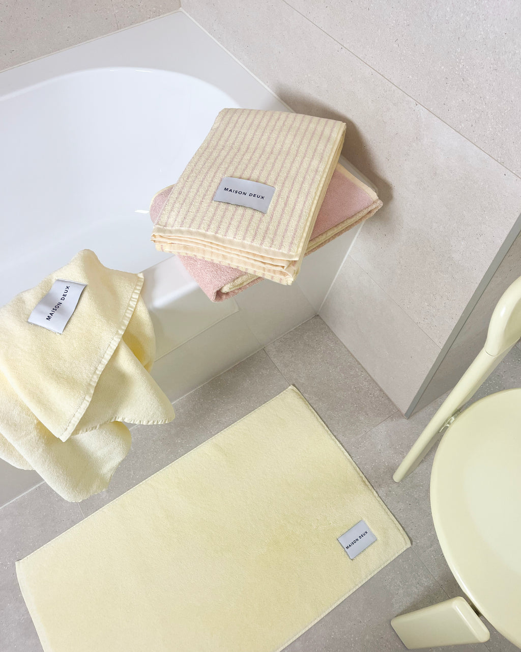 Solid butter yellow towel and bath mat styled with striped and gradient towels