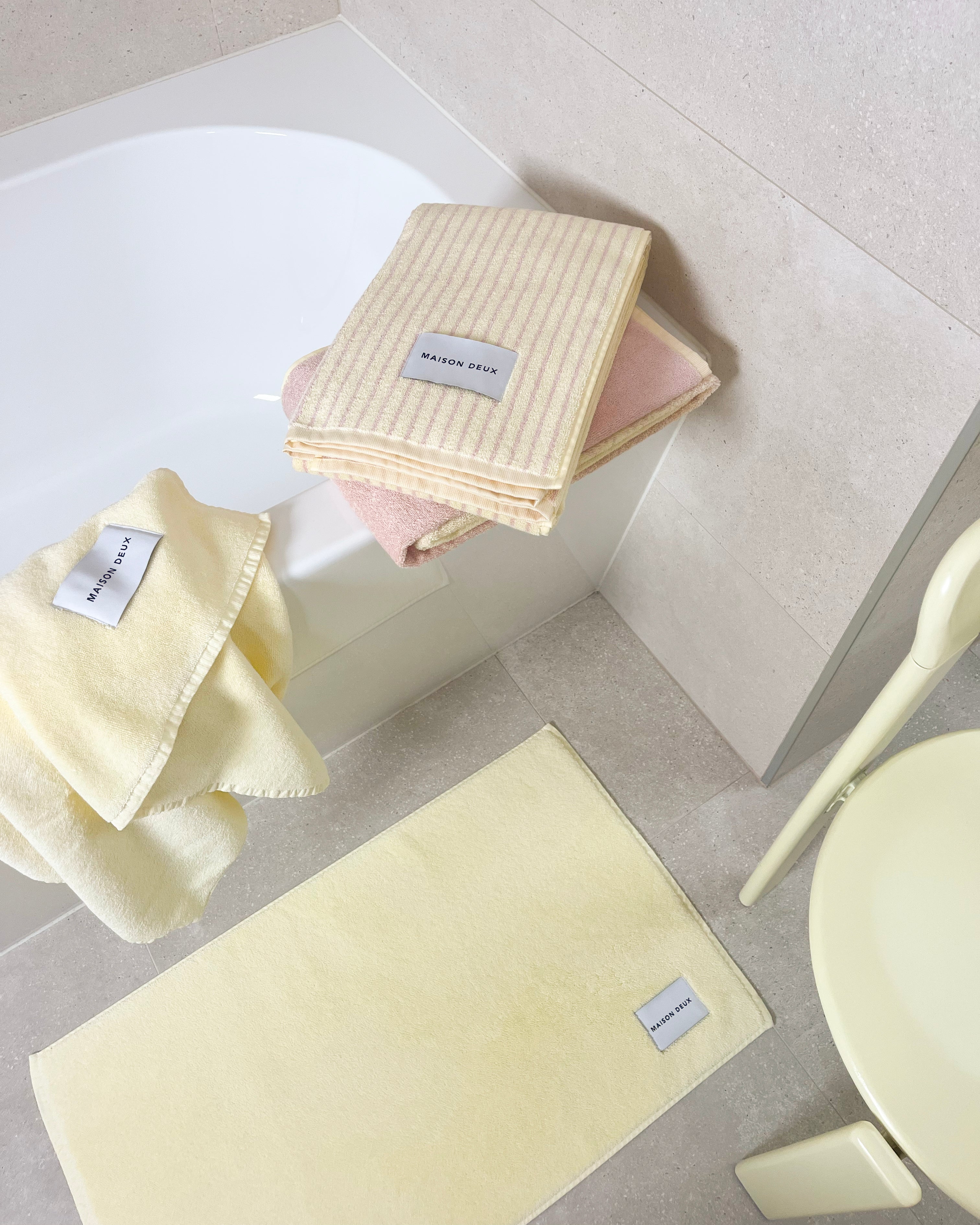 Solid butter yellow towel and bath mat styled with striped and gradient towels