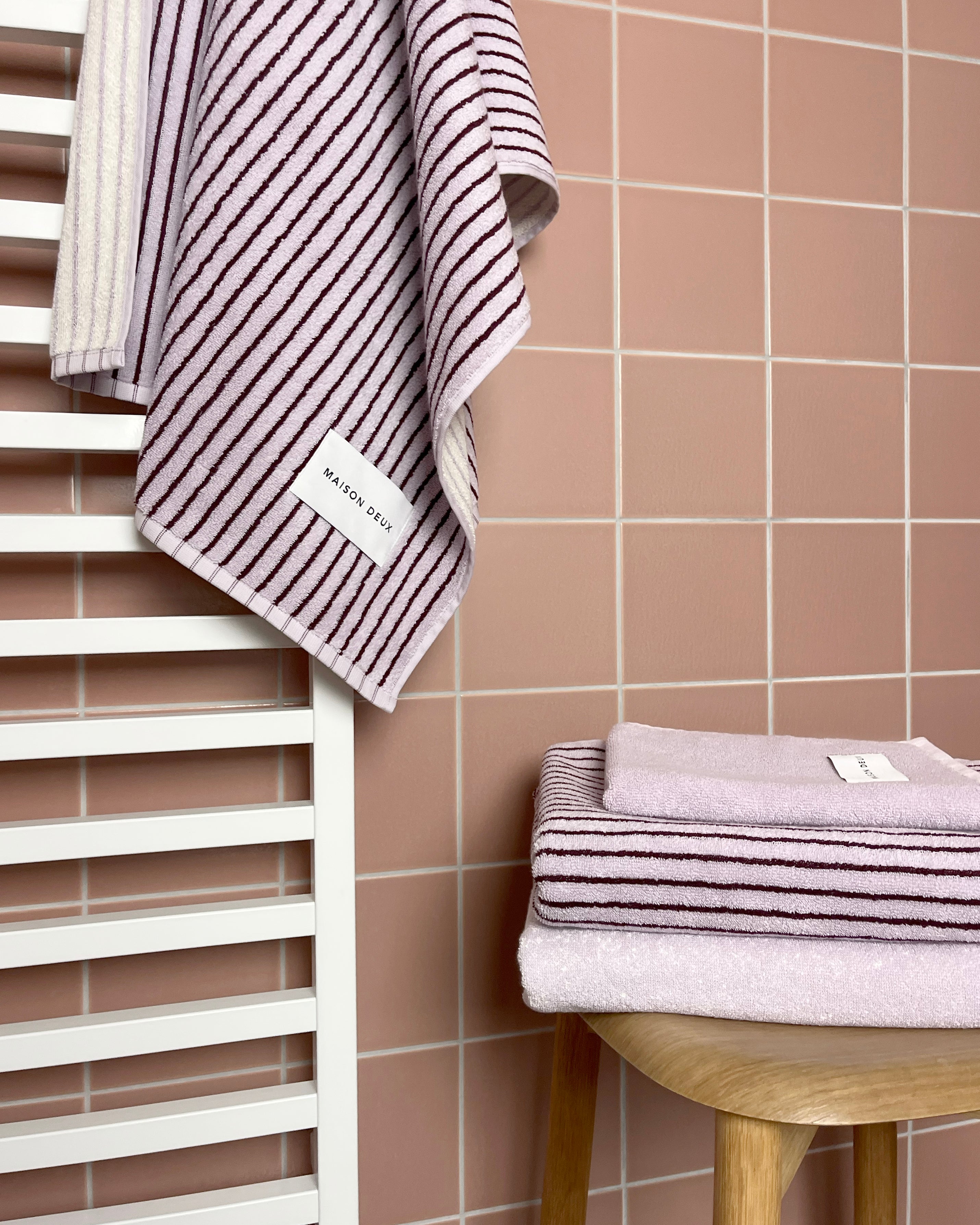 Solid lilac towel folded with lilac bordo striped towel on stool