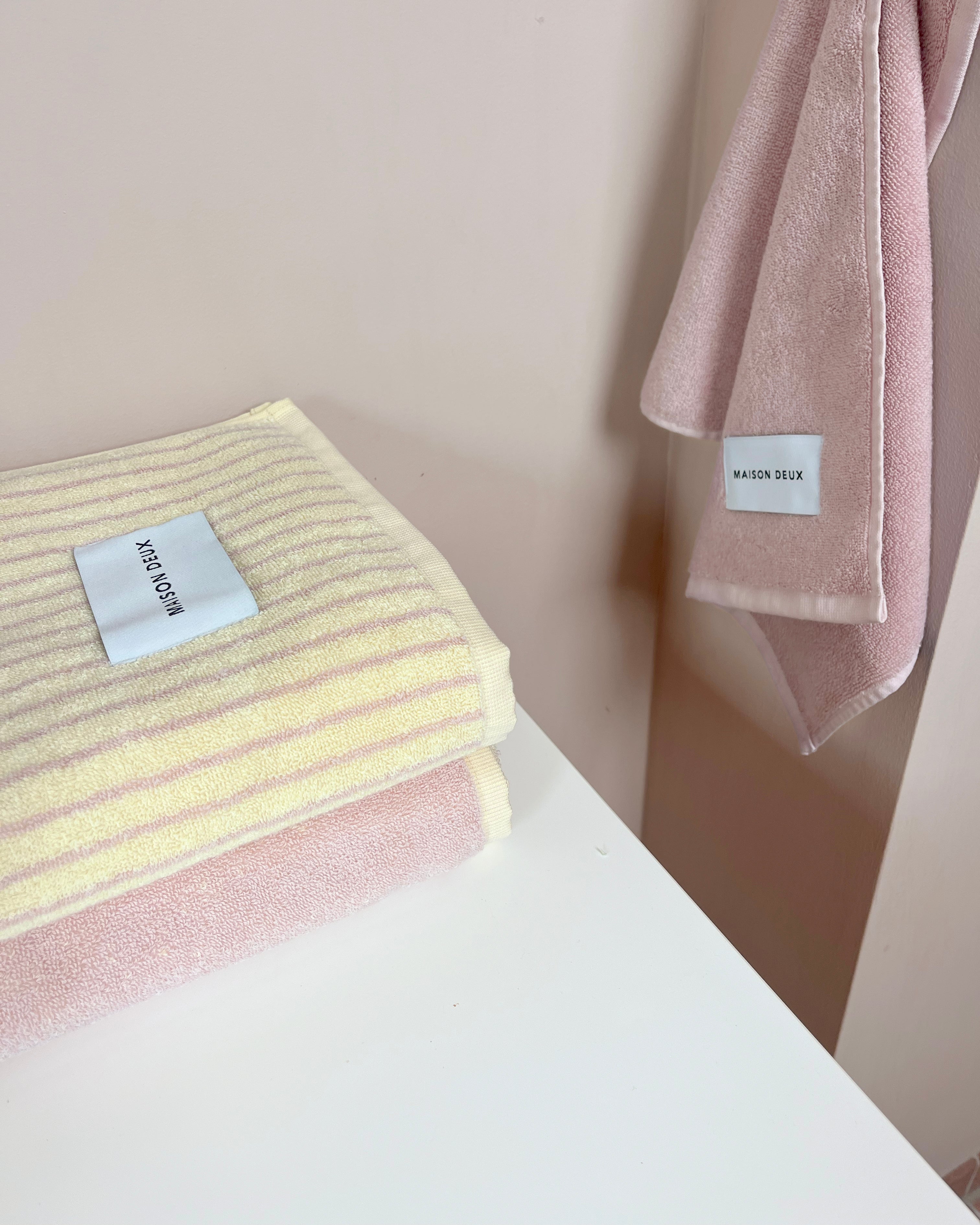 Solid pink towel hanging beside folded striped and gradient towels