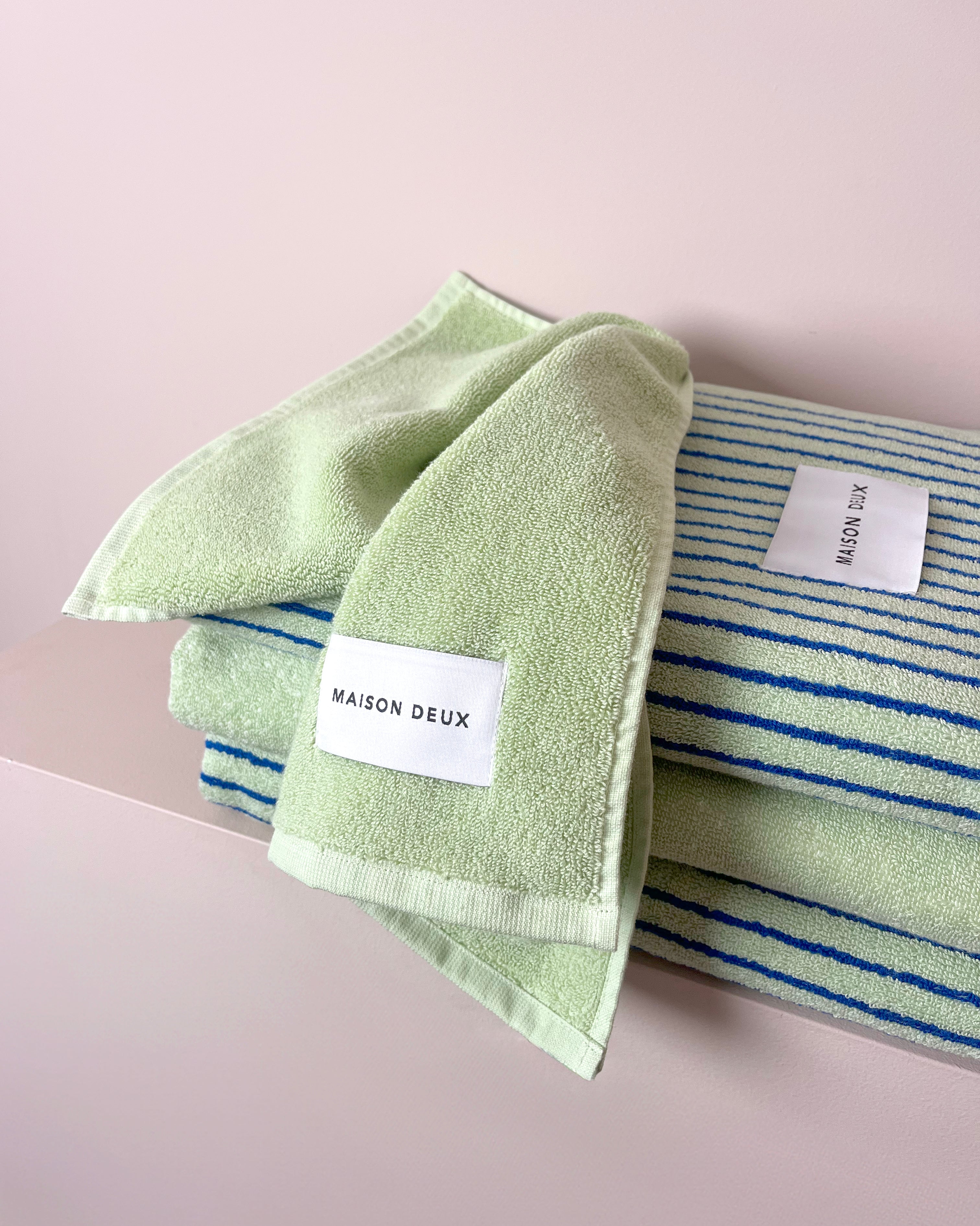 Solid sage green towel folded beside striped towel