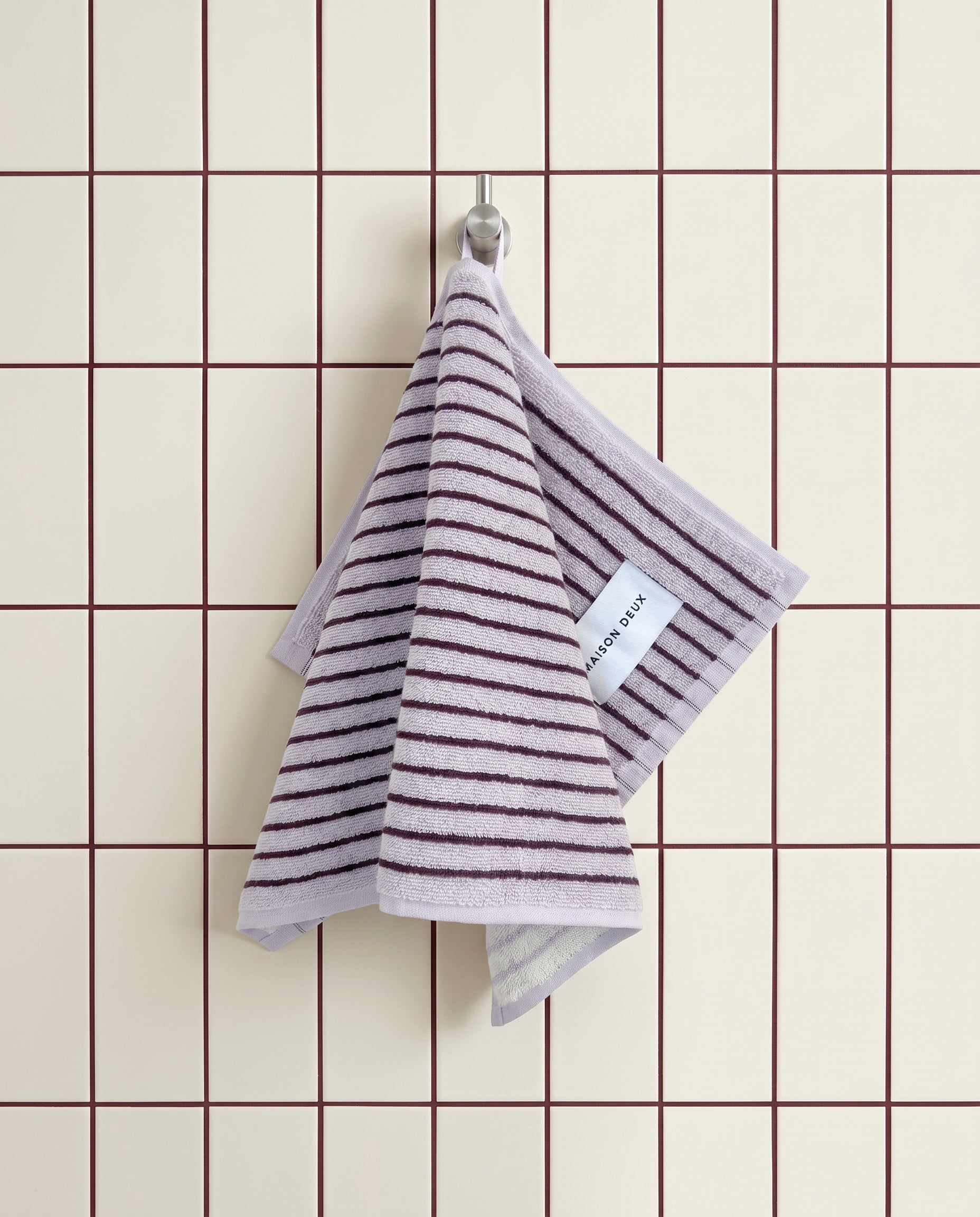 Lilac bordo striped guest towel hanging on hook against tiled wall