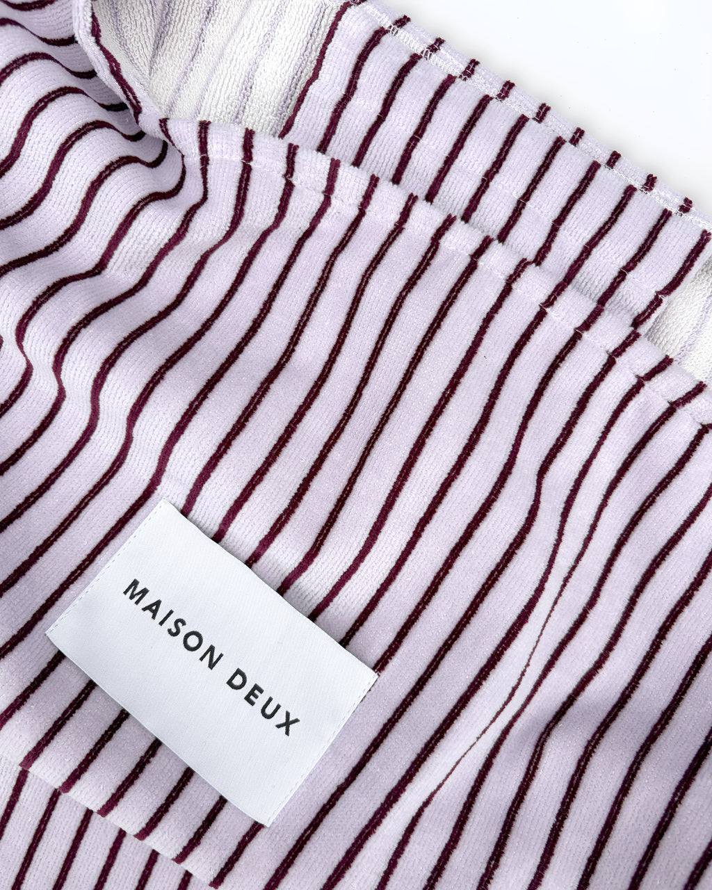 Close-up of lilac and bordeaux striped terry bag fabric with woven label