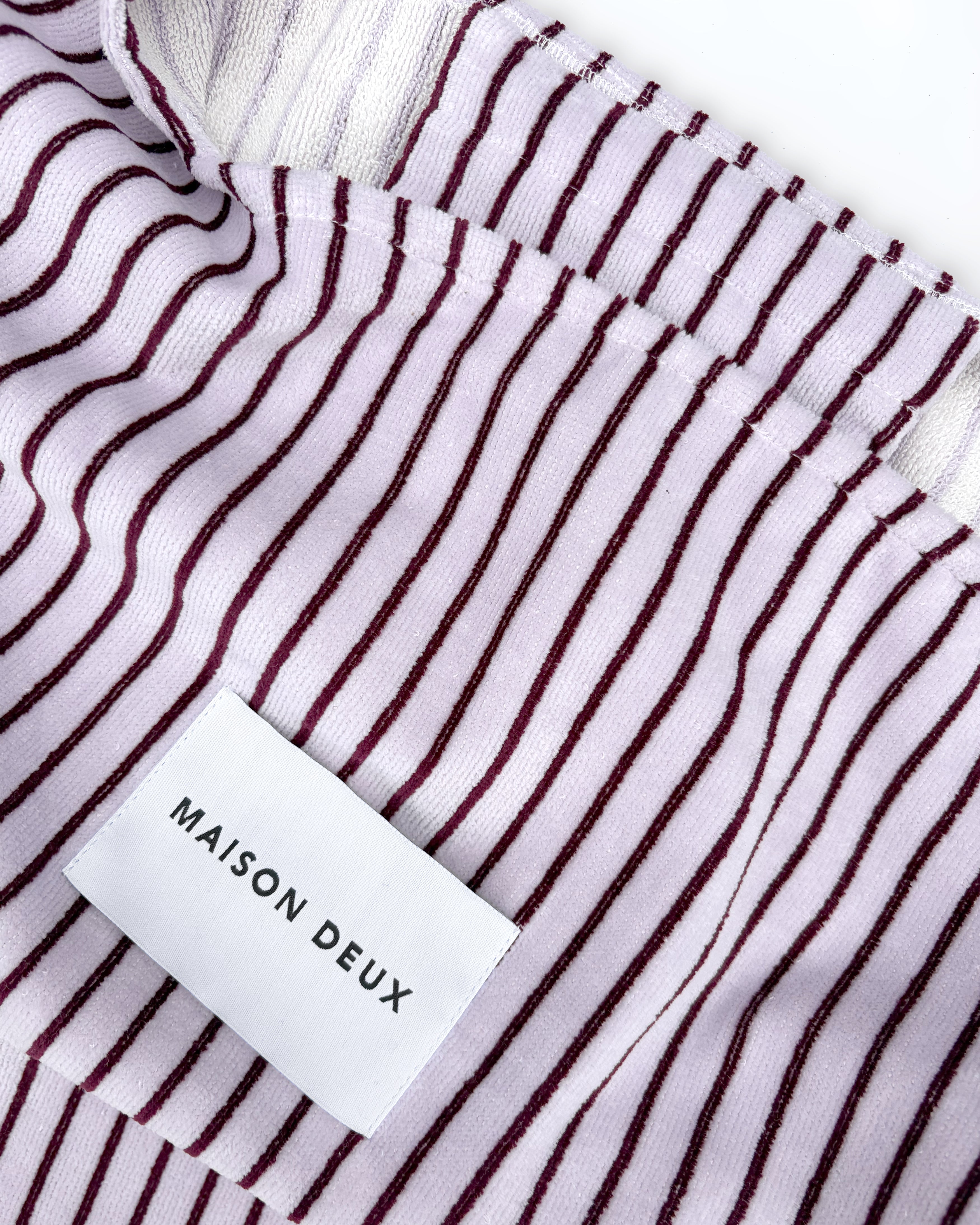 Close-up of lilac and bordeaux striped terry bag fabric with woven label