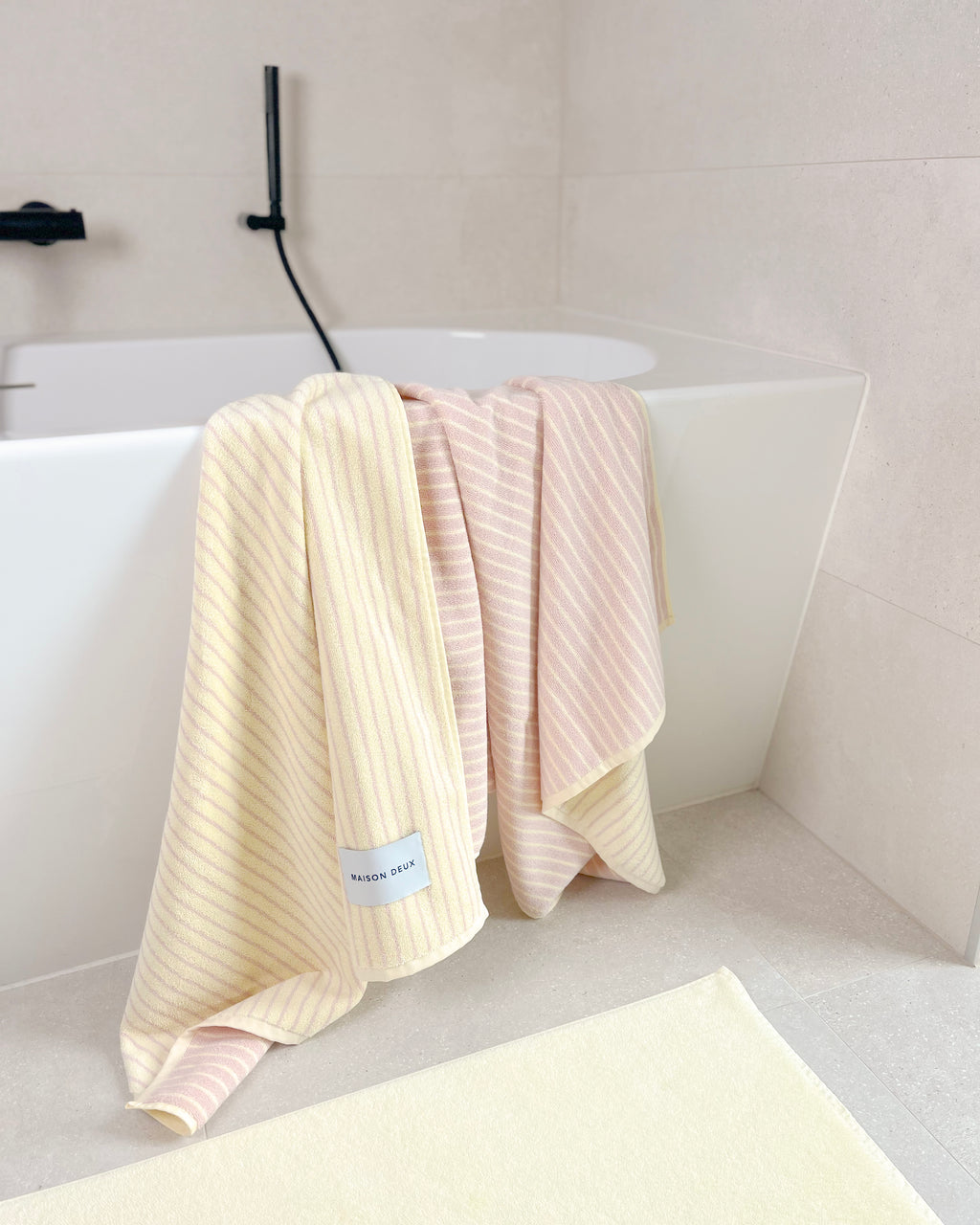 Butter yellow and pink striped towel hanging over bathtub edge