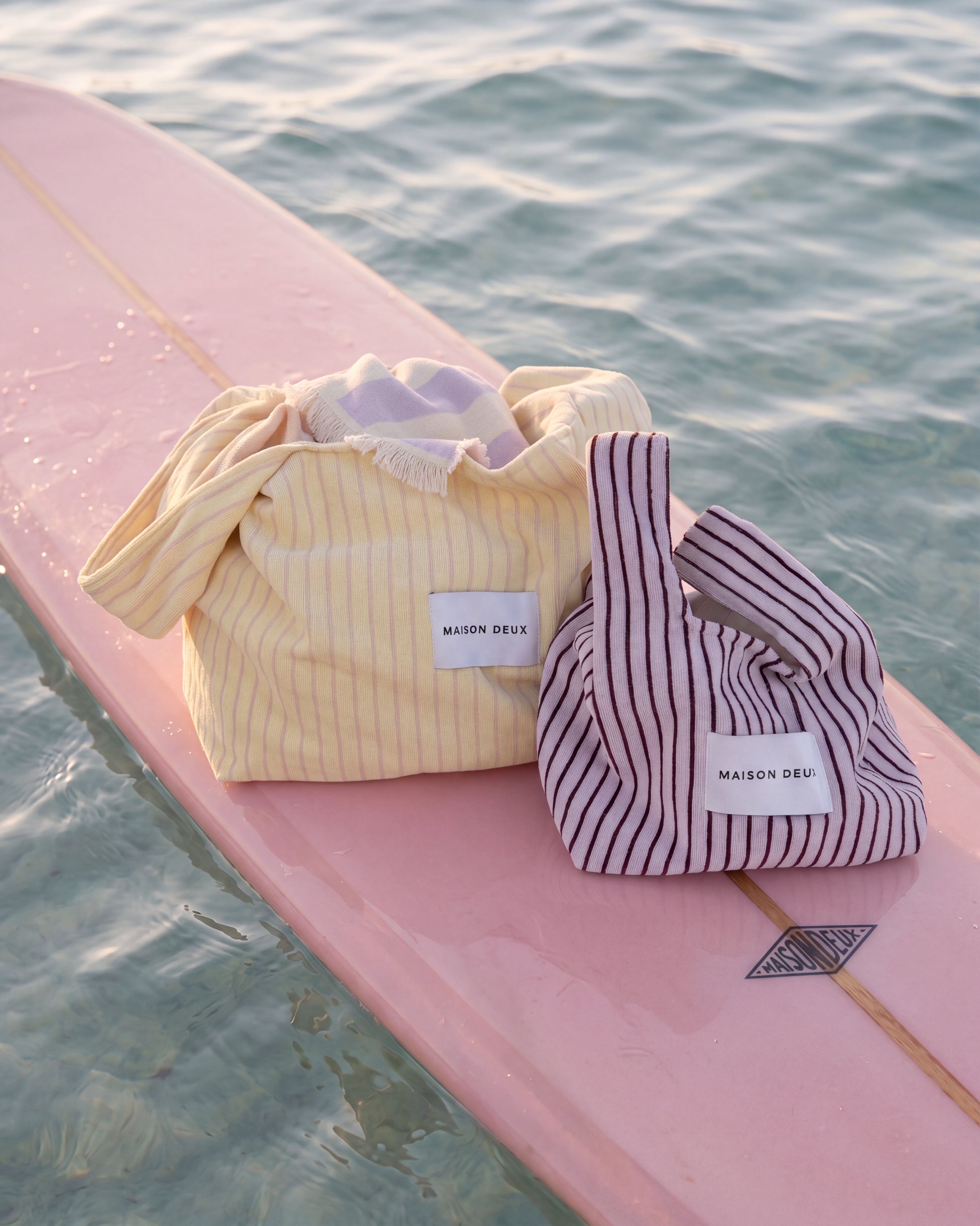 Lilac and bordo mini terry beach bag styled with butter yellow bag on pink surfboard